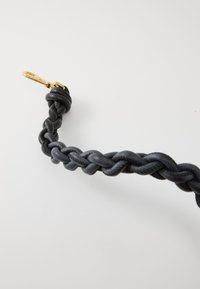 Correa de cuero trenzado negro con una textura suave y un clip metálico dorado para sujeción.