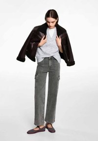 Brun shearling-fodrad jacka, grå kabelstickad tröja, grå cargobyxor och svarta vävda flats med röda detaljer. Avslappnad lager-på-lager outfit.