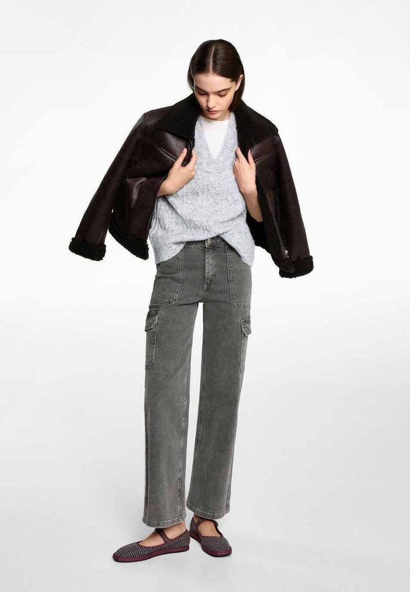 Brun shearling-fodrad jacka, grå kabelstickad tröja, grå cargobyxor och svarta vävda flats med röda detaljer. Avslappnad lager-på-lager outfit.