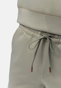 Pantalon de jogging gris clair en tissu doux, doté d'une taille élastique, d'un cordon de serrage réglable avec des embouts rouges, et de poches latérales.