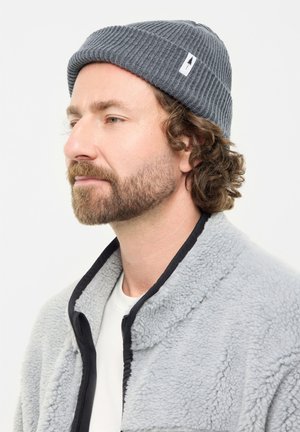 Gray ribbed knit beanie features a rolled cuff and a small white tag. The model wears a gray fleece jacket with a black trim.