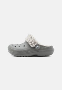 Sabot gris avec une doublure blanche en fourrure, doté de trous de ventilation, d'un bouton logo circulaire et d'une semelle texturée pour une meilleure adhérence.