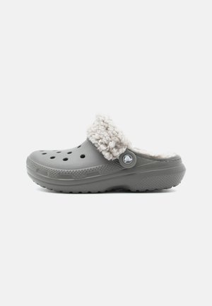 Gray clog with a fuzzy white lining, featuring ventilation holes, a circular logo button, and a textured sole for grip.