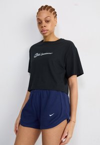 Črna kratka majica s tekstom "Sportwear", v kombinaciji z modrimi rebrastimi kratkimi hlačami, ki imajo bel Nike logo na robu.