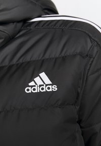 Černá péřová bunda s hladkým povrchem, s bílým logem Adidas a ikonickými třemi pruhy na rameni.