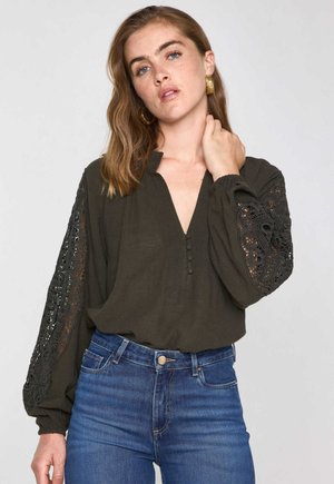 Blusa verde scuro con scollo a V, dettagli con bottoni e maniche lunghe con eleganti accenti in pizzo nero. Tessuto morbido e testurizzato.