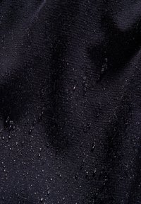 Tissu noir avec une texture lisse, présentant des gouttes d'eau à la surface, indiquant un matériau résistant à l'eau ou enduit.
