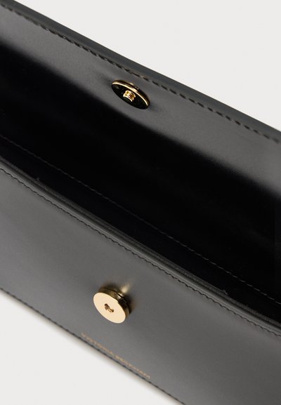 Μαύρο δερμάτινο πορτοφόλι με κλείσιμο με μαγνήτη σε χρυσό τόνο, ανοιχτό για να εμφανίζεται το λείο εσωτερικό και οι ραμμένες άκρες.