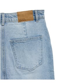 Poche de jean en denim bleu clair avec des coutures visibles et un patch en cuir marron portant l'étiquette "VERO MODA WE DO DENIM" sur la ceinture.