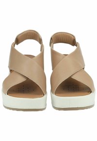 Sandali in pelle beige con cinturini incrociati, punta aperta, soletta imbottita e base piatta bianca. Texture liscia e design minimale.