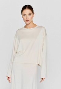 Beige Langarmtop aus weichem, leichtem Stoff mit lockerer Passform und rundem Ausschnitt, kombiniert mit einem passenden Rock.