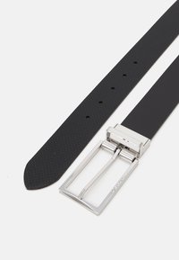 Cintura nera in gomma con superficie texturizzata e una fibbia metallica rettangolare argentata. Dotata di più fori per la regolazione della taglia.