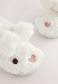 Hvide plysprinseskildpadde-tøfler med runde ører, en blød tekstur og hjerteformede accenter i pink og brun på forsiden.