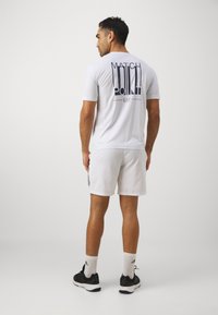 Balta trumpa sportinė marškinėliai su užrašu "MATCH POINT" ir logotipu ant nugaros, derinami su baltais šortais, juodais batais ir baltais kojiniais.