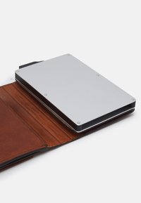 Porte-cartes en métal avec une finition argentée, fixé par quatre petites vis, placé à l'intérieur d'un portefeuille en cuir marron avec une texture visible et des emplacements pour cartes.