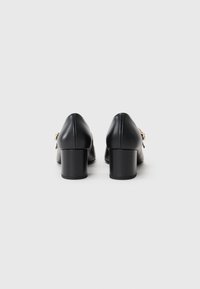Black leather block-heeled shoes with a pointed toe, featuring gold hardware accents on the side. Smooth texture with a polished finish.
