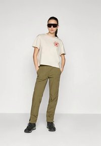 T-shirt bege de manga curta com bordado floral no peito, combinada com calças afuniladas verde-oliva e botas pretas com atacadores.