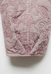 Tessuto trapuntato rosa con motivi floreali e fogliari. Texture liscia con cuciture in rilievo che creano un effetto tridimensionale.