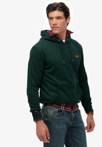 Donkergroen hoodie met een voorkraag, met een contrasterend rood geruit shirt zichtbaar bij de kraag en manchet.