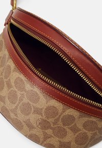 Borsa di tessuto marrone con motivo, dettagli in pelle rossa e cerniere dorate. L'interno è color bordeaux, mostrando una consistenza liscia.