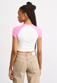 Camiseta recortada de cuerpo blanco y mangas raglán rosas, combinada con pantalones de tiro alto beige con detalles desgastados y bolsillos traseros.
