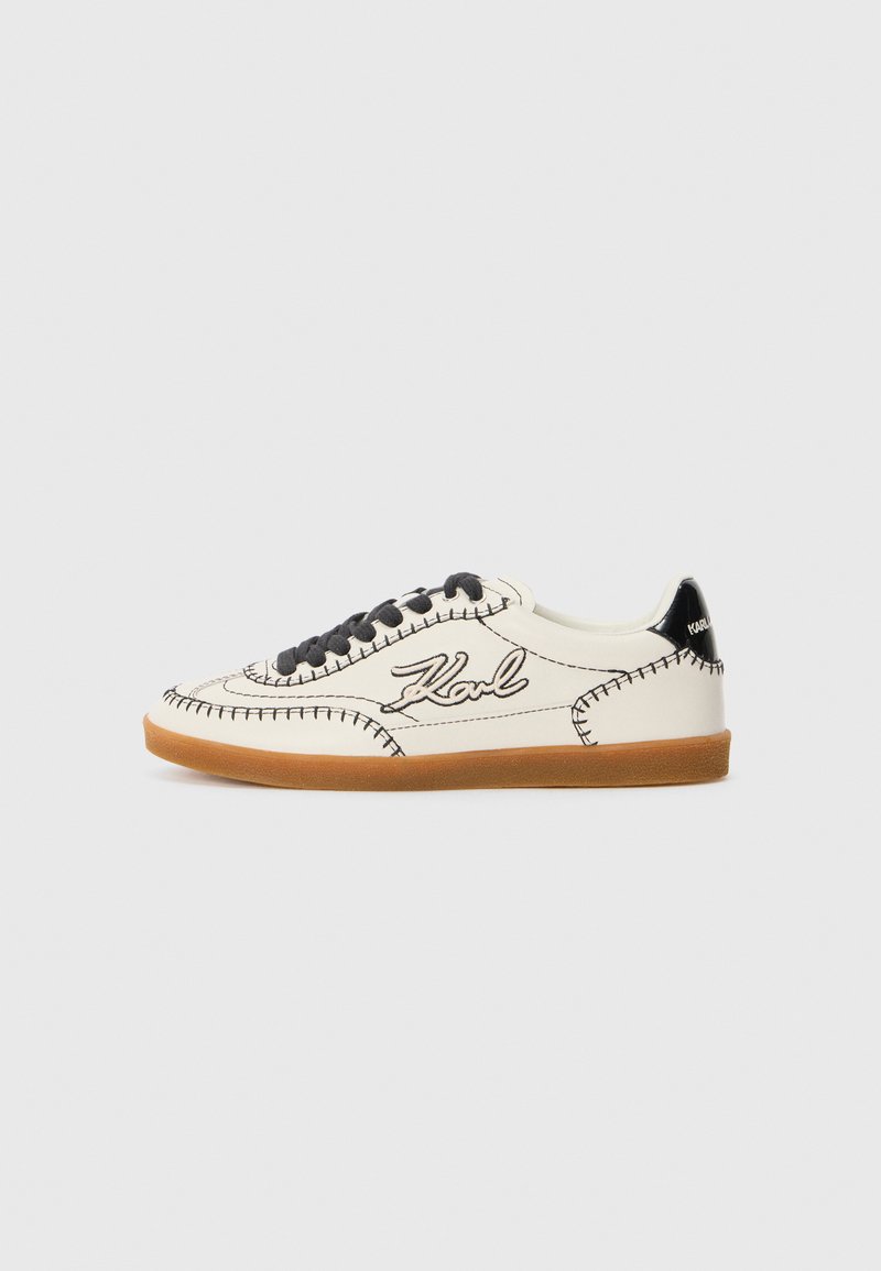 Sneakers with a cream leather upper, black stitching, and black laces. Features a brown rubber sole and a black heel tab with logo.