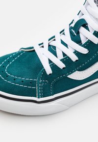 Tummansininen mokkasiinikenkä valkoisilla nauhoilla ja ompeleilla. Varustettu musta-valkoisella kumipohjalla ja ikonilla sivulogo-yksityiskohdalla.