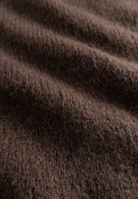 Rjava tkanina z izrazito teksturo in mehko, puhasto površino. Površina prikazuje vodoravne grebene, kar kaže na pleteno ali tkanje konstrukcijo.