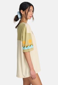 T-shirt oversize à manches courtes en beige et vert avec des motifs de soleil et de vagues, présentant une coupe décontractée et une texture en coton doux.