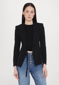 Fekete szabott blazer, átlapolt gallérral és nyitott elülső résszel. Fekete textúrájú toppal és magas derekú kék farmernadrággal párosítva, arany gombokkal.