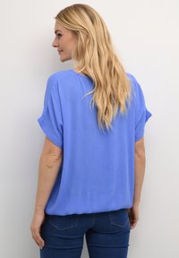 Maglietta morbida, a maniche corte e dal taglio ampio, realizzata in tessuto azzurro chiaro, con scollatura a girocollo e superficie morbida, abbinata a jeans scuri.