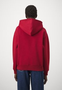 Rotkapuzenpullover mit gerippten Bündchen und Saum, aus strukturiertem Stoff. Sichtbare Nähte und eine lockere Passform, kombiniert mit lockeren blauen Jeans.
