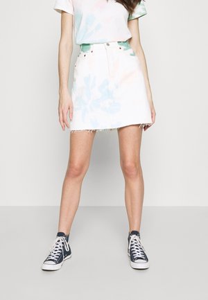Femme portant une jupe tie-dye claire avec un ourlet effiloché, un t-shirt tie-dye assorti et des baskets montantes noires sur un fond uni.