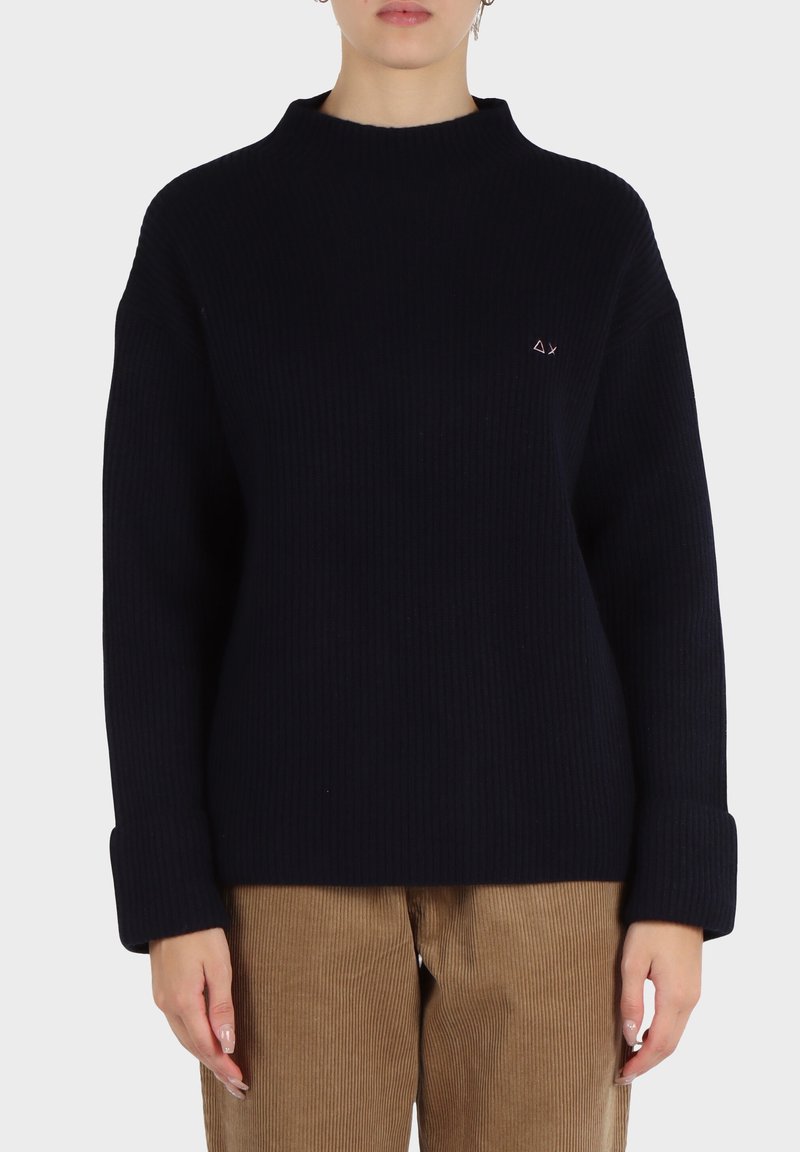 Maglione blu navy a costine con collo alto, vestibilità oversize e un piccolo logo ricamato sul lato sinistro. Tessuto testurizzato con maniche lunghe.