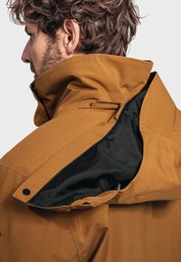 Brown waterproof jacket with a high collar, featuring a black inner lining and a zippered pocket. Smooth texture, minimalist design.