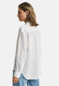 Witte linnen shirt met lange mouwen, knoopmanchetten en een relaxte pasvorm. De achterkant heeft een subtiele plooi en een afgeronde zoom.