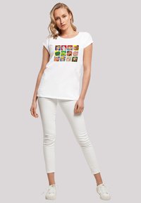 White short-sleeved t-shirt featuring a colorful grid of cartoon character faces; paired with fitted white pants and white shoes.