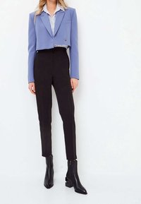 Blazer blu tagliato con rever a incasso, abbinato a pantaloni neri aderenti e stivaletti neri con tacco a blocco. Camicia a righe sotto.