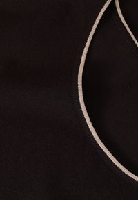 Gros plan d'un tissu noir avec un bord courbé bordé de blanc, montrant la texture et les détails de la couture.