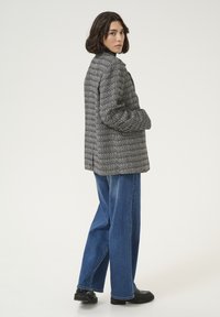 Black and white houndstooth blazer with a structured shape, single-breasted design, and vented back, paired with wide-leg blue denim jeans.