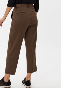 Pantalons marron à rayures avec une taille haute, longueur cropped et deux poches arrière. Associés à des baskets noires à lacets.