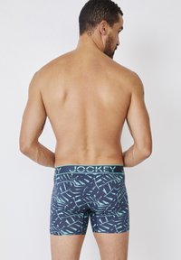 Jockey boxershorts in marineblauw met een lichtgroen abstract patroon. De elastische tailleband heeft de merknaam in hoofdletters.