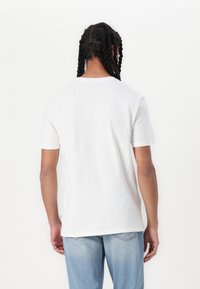 Hvit bomulls t-skjorte med korte ermer, rund hals og en avslappet passform. Brukt med lyseblå jeans.