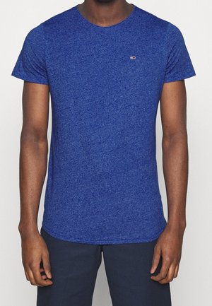 Homme portant un t-shirt bleu chiné à manches courtes ajusté avec un petit logo rectangulaire sur le côté gauche de la poitrine.