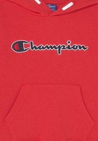 Roter Champion-Hoodie mit einer vorderen Kängurutasche und dem gestickten Logo der Marke in Schwarz und Weiß auf der Brust.