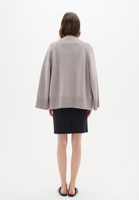 Pull en tricot gris clair oversize avec un large col et un ourlet côtelé. Porté sur une jupe noire, mettant en valeur une silhouette décontractée et carrée.