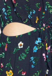 Blommig klänning med marin bakgrund, med utskurna sidor och dragsko. Mönstret inkluderar livliga blommor i rosa, blått, gult och vitt.