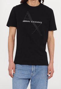 Svart bomullströja med en stor, texturerad "AX"-logotyp och "ARMANI EXCHANGE" i vitt, kortärmad och med en klassisk passform.