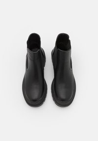 Czarne skórzane botki za kostkę z elastycznymi bocznymi panelami, zaokrąglonymi nosekiem i teksturowanymi gumowymi podeszwami. Gładkie wykończenie z minimalnymi detalami przeszycia.