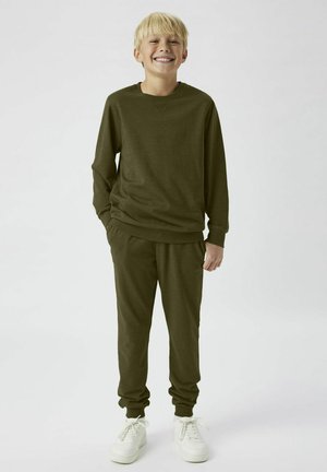 Olivgrüner Fleece-Sweatshirt mit langen Ärmeln und passenden Jogginghosen; beide verfügen über elastische Bündchen und eine lockere Passform, kombiniert mit weißen Sneakers.